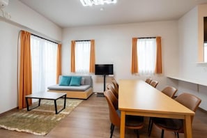 A modern hotel room with a wooden dining table, a sofa, and a flat-screen TV. - KAIGAN HAJIME HUB (Tokyo)