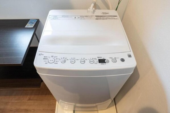 A front view of a white washing machine with control panel, placed on a wooden floor against a wall. - KAIGAN HAJIME HUB (Tokyo)