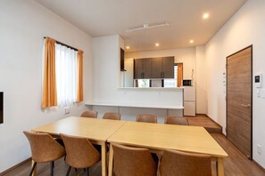 A modern dining area with a long table and chairs, a kitchen in the background, and a door on the right. - KAIGAN HAJIME HUB (Tokyo)