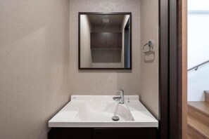 A bathroom with a white sink, a mirror, and a wooden staircase in the background.