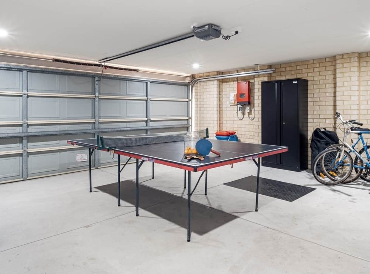 Un garaje con mesa de ping-pong, bicicleta y un refrigerador negro.