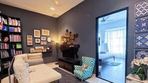 Un salón moderno con un sofá, un televisor, una estantería y vistas al exterior.