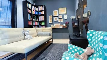 Una sala de estar con sofá, una silla estampada con lunares, una estantería y un televisor montado en la pared.