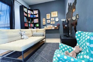 Un salon avec un canapé, un fauteuil à motifs à pois, une bibliothèque et un téléviseur fixé au mur.