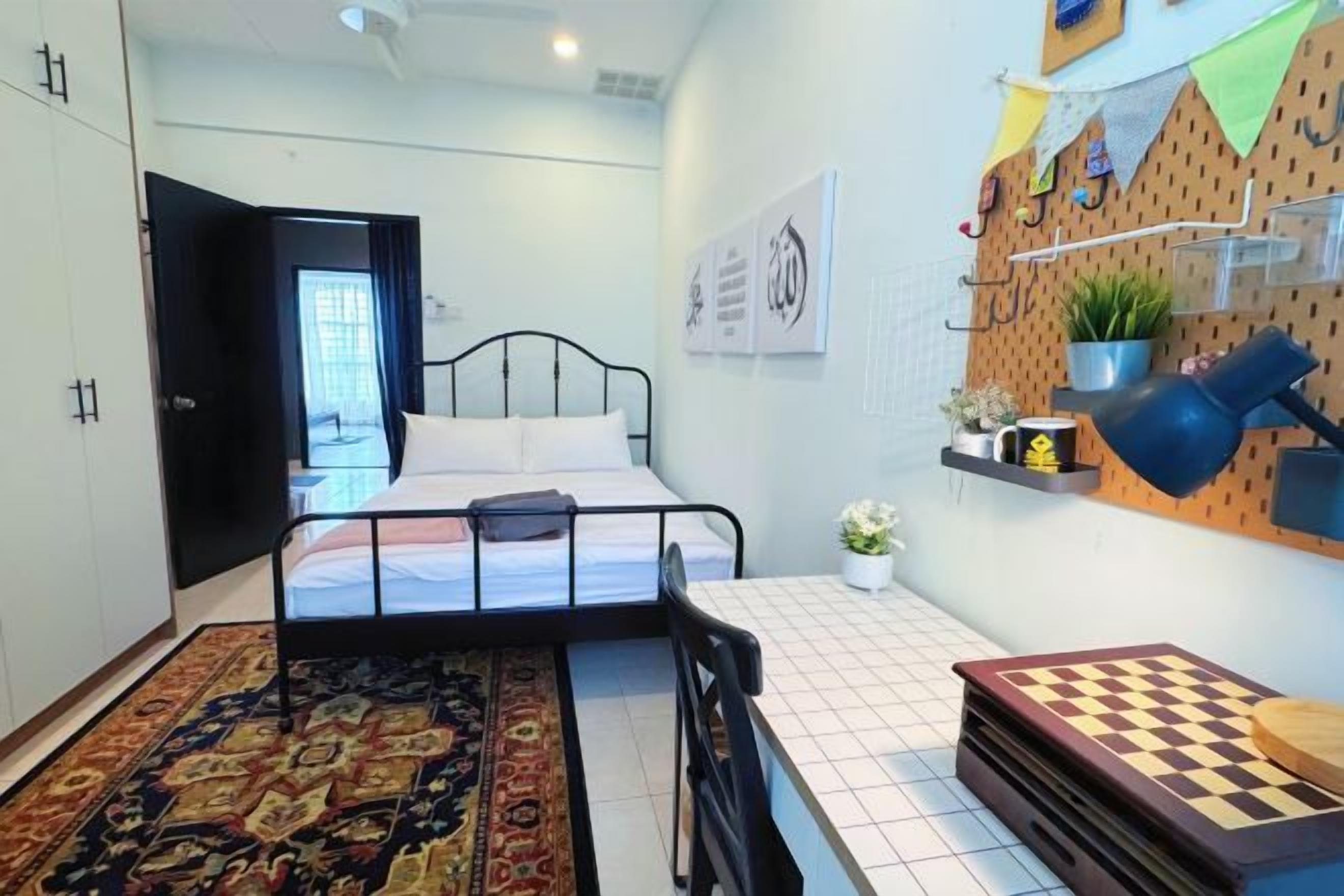 A bedroom with a bed, a desk, a chair, a chessboard, a rug, and a wall-mounted shelf with plants.