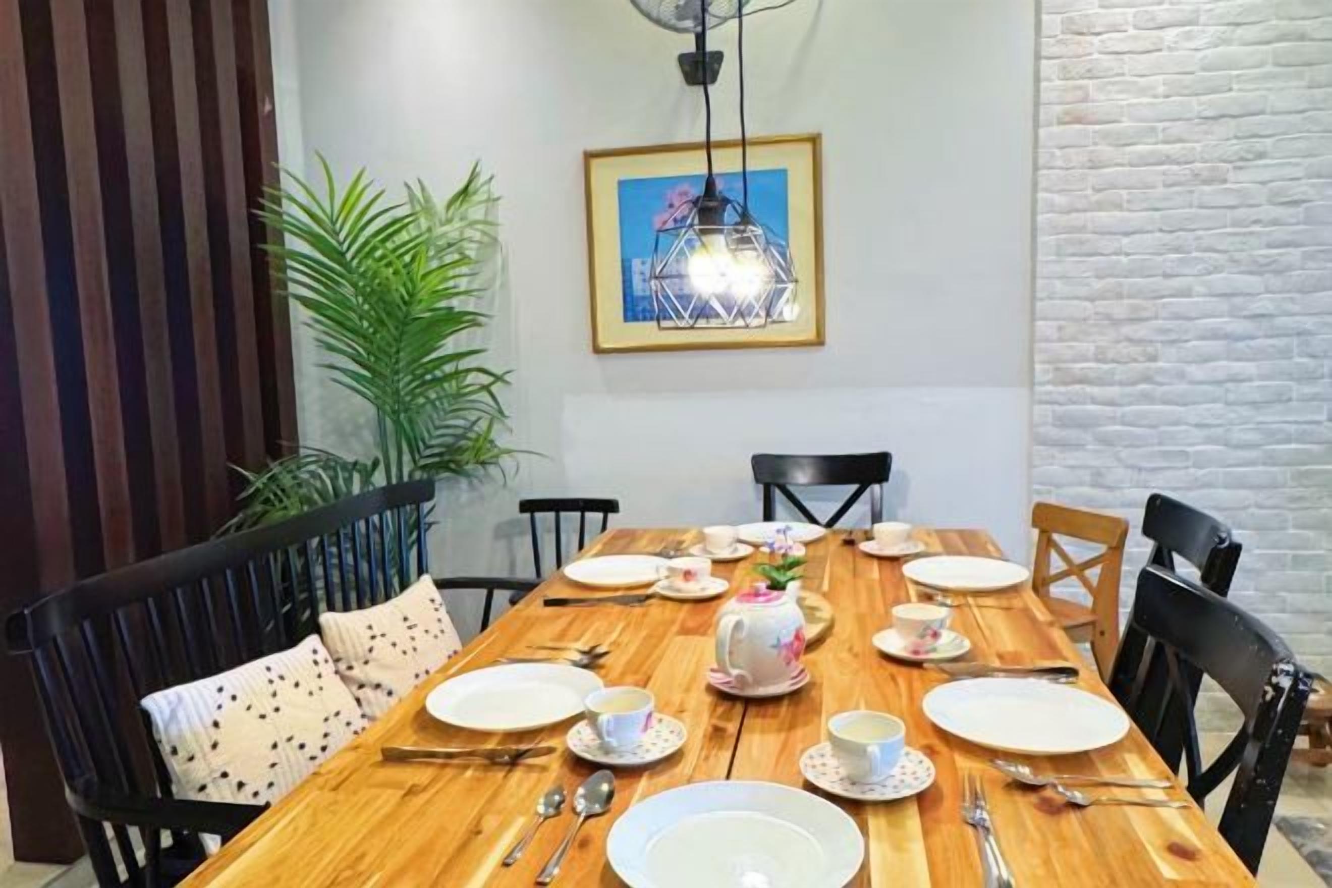 A dining area with a wooden table set for four, chairs, a potted plant, and a framed picture on the wall.