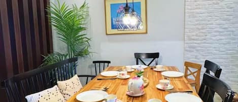 A dining area with a wooden table set for four, chairs, a potted plant, and a framed picture on the wall.