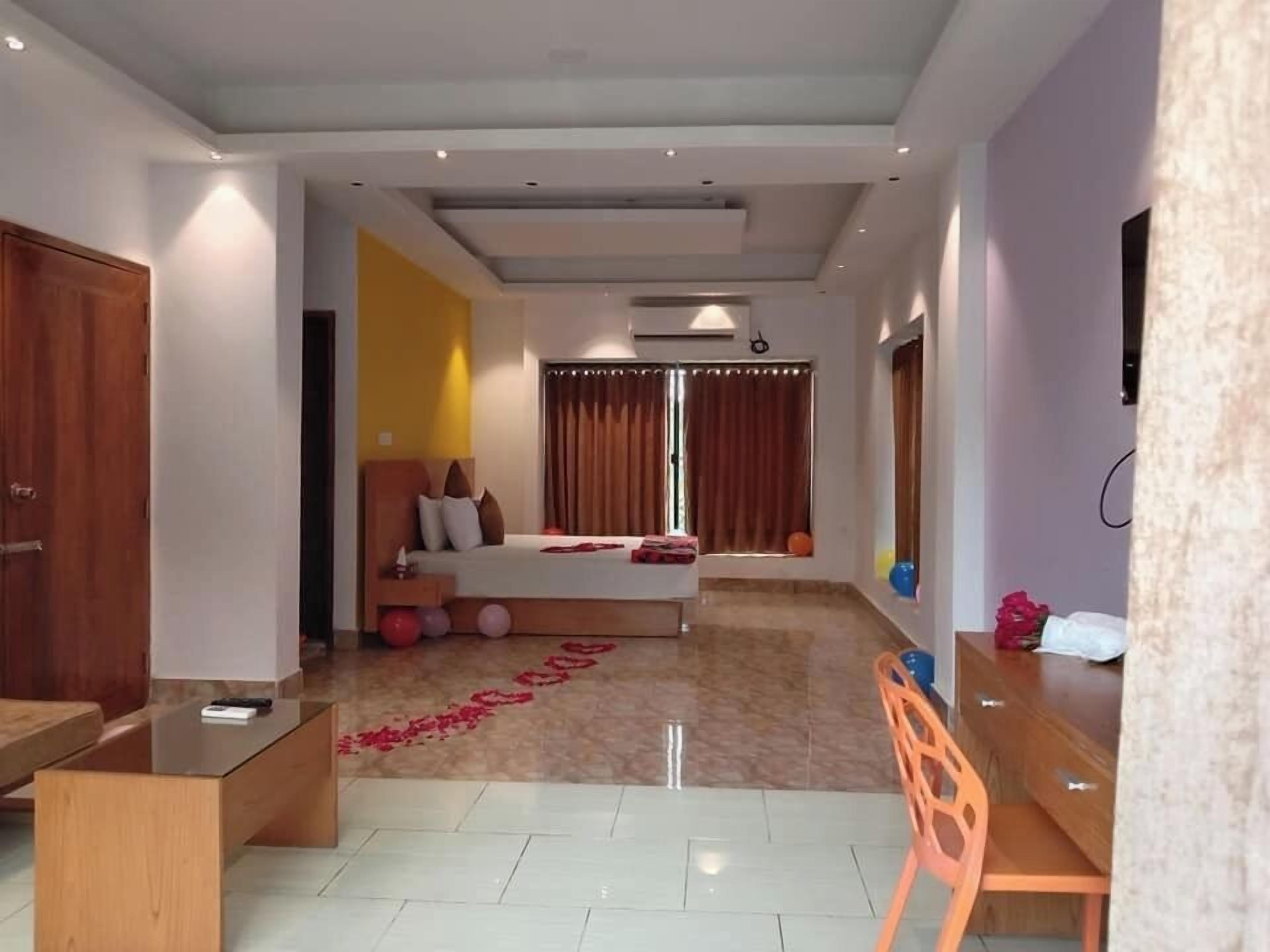 A modern hotel room with a bed, a desk, and a chair. There is a window with curtains and a ceiling fan.