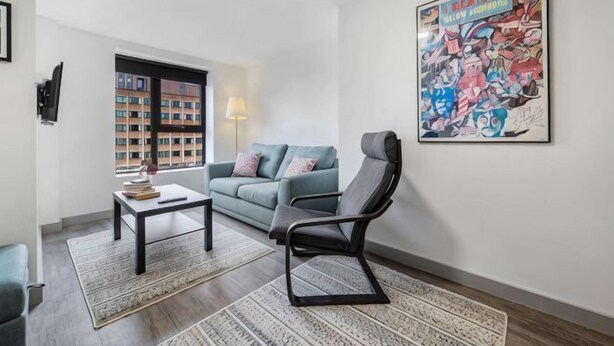 Ein Wohnzimmer mit Sofa, Sessel, Couchtisch, Teppich, Lampe und einem großen Poster an der Wand.