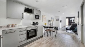Eine moderne Küche mit Edelstahlgeräten, ein Essbereich mit Tisch und Stühlen sowie ein Wohnbereich mit Sofa und Couchtisch.