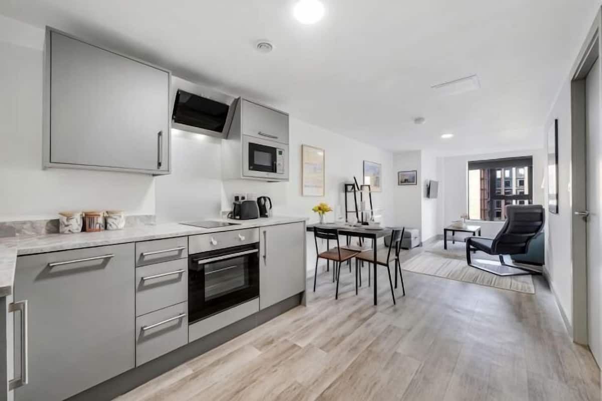 A modern kitchen with stainless steel appliances, a dining area with a table and chairs, and a living space with a sofa and a coffee table.
