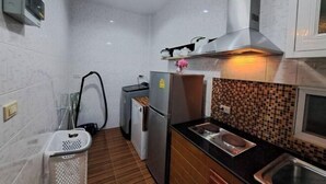A compact kitchen with white tiled walls, a wooden floor, a stainless steel sink, and a refrigerator. - Bluepool Villa Pattaya (Sattahip)