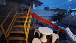 A wooden staircase with a red slide, a round table, and two stools in a courtyard. - Bluepool Villa Pattaya (Sattahip)