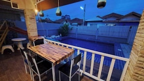 A balcony with a wooden table and chairs, a small pool, and a white fence. - Bluepool Villa Pattaya (Sattahip)