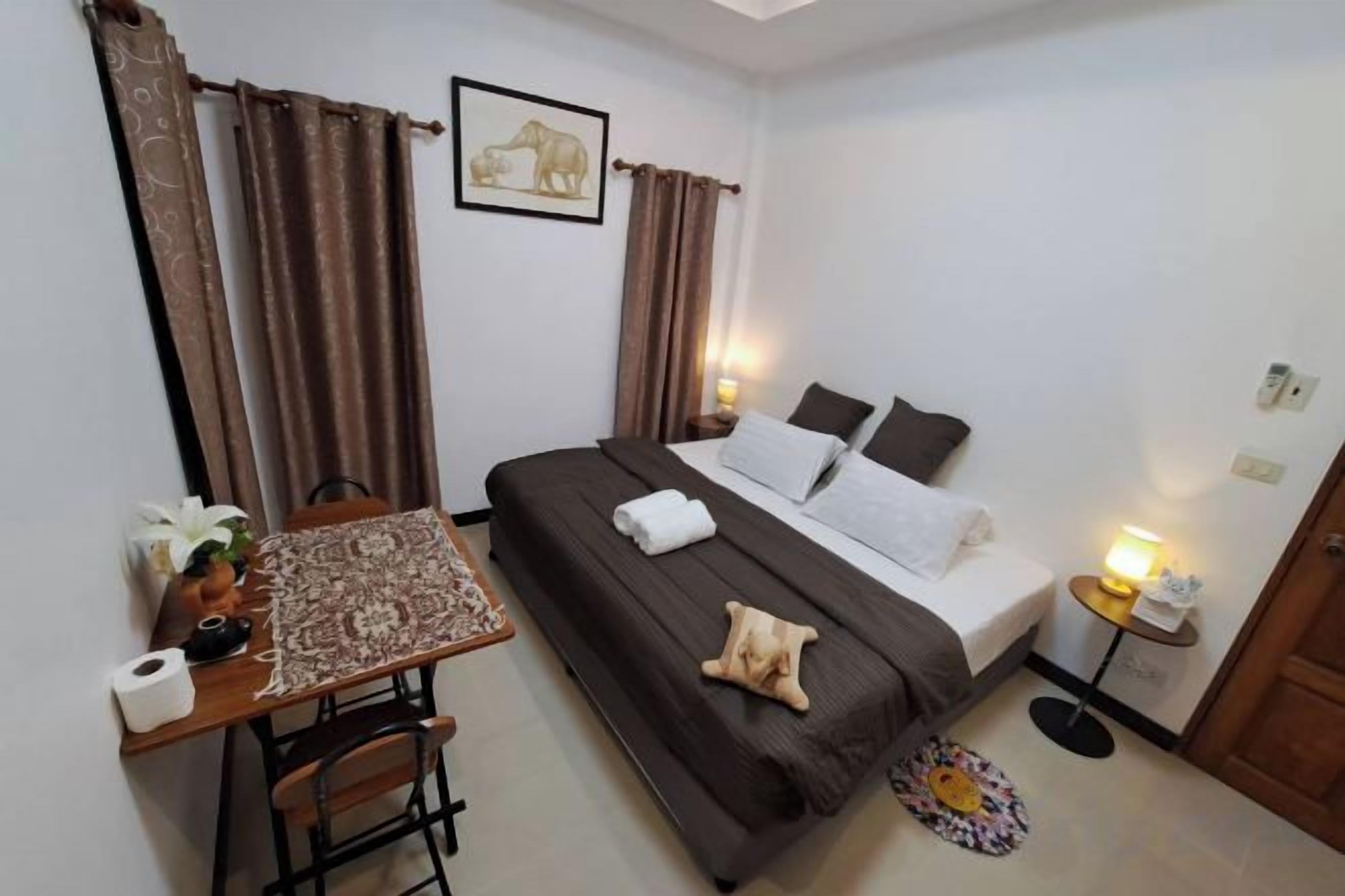 A bedroom with a bed, bedside table, lamp, curtains, and a framed picture on the wall.