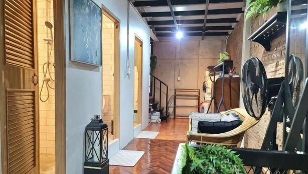 A hallway with a wooden floor, a black lantern, a cushioned chair, and a wall-mounted fan. - MEEMAW'S HOUSE (Bangkok)