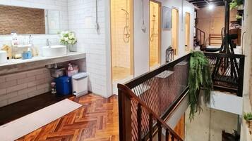 A hotel bathroom with a large mirror, white tiles, and a wooden floor.