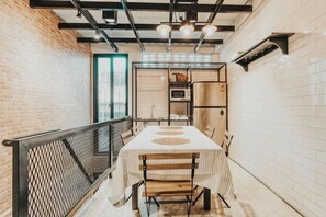 A narrow hallway with a table and chairs, a metal railing, and a brick wall.
