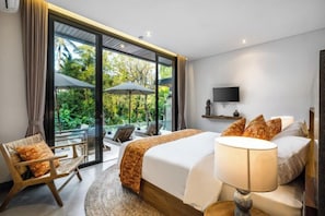 A hotel room with a large bed, a TV, a sofa, and a balcony with a view of greenery. - Villa Golden Lion by BaliSuperHost (Bali)