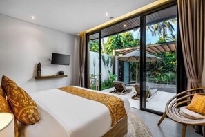 Une chambre moderne avec un grand lit, un téléviseur fixé au mur et une porte-fenêtre coulissante donnant sur un patio aménagé avec du mobilier d’extérieur.