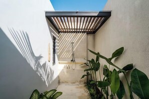 Een smalle buitenruimte met een douche, een houten pergola en planten in potten.