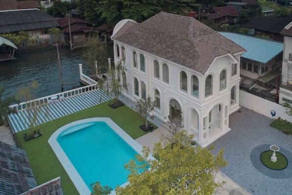 A white building with a swimming pool, surrounded by a garden and a body of water. - Arpo Pool Villa Riverside Bangkok (Bangkok)
