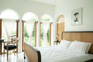 Ein Schlafzimmer mit einem Bett, einem Sessel und einem Schreibtisch. Es gibt drei Fenster mit Vorhängen.