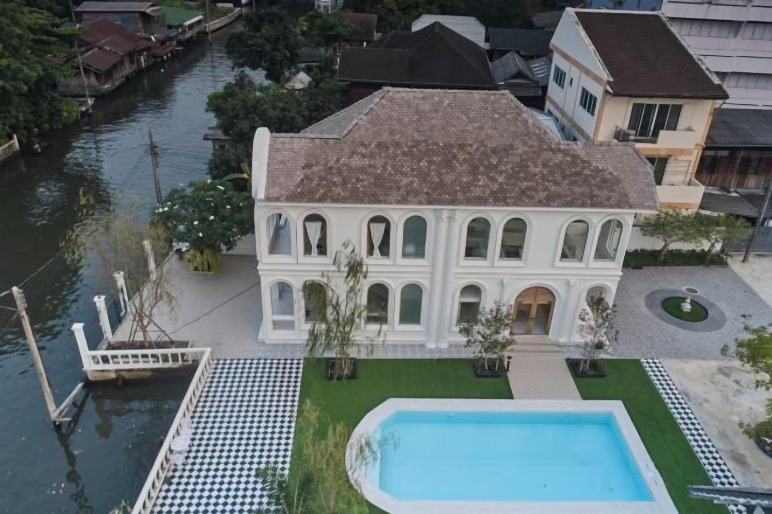 A white villa with a swimming pool, located near a canal.