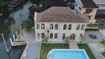 A white villa with a swimming pool, located near a canal.