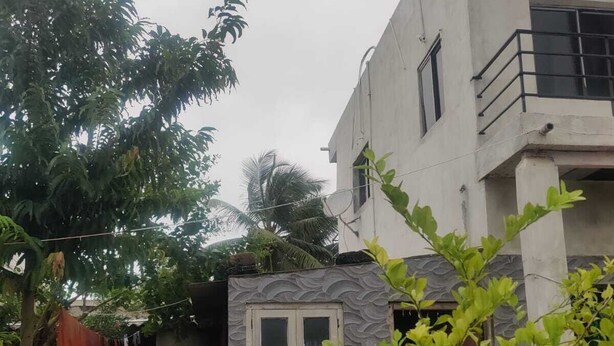 Zona residencial amb un edifici de dos pisos, un petit jardí amb plantes verdes i una porta blanca.