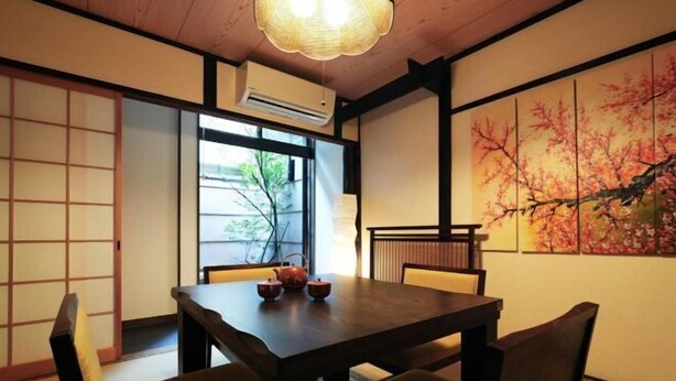 A traditional Japanese room with tatami flooring, a wooden table with a tea set, a shoji screen, and a cherry blossom painting.