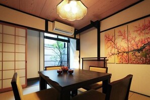 A traditional Japanese room with tatami flooring, a wooden table with a tea set, a shoji screen, and a cherry blossom painting.