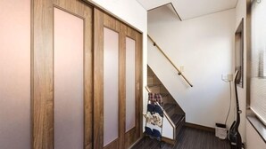A narrow hallway with wooden doors, a staircase, and a window with blinds.