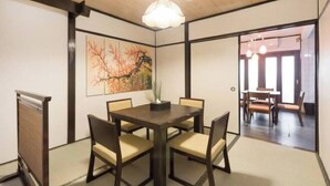 A traditional Japanese-style room with tatami flooring, a dark wooden table with chairs, a hanging light fixture, and a painting on the wall.