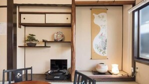 A traditional Japanese room with tatami flooring, a low table, chairs, a shelf with decorative items, a television, and a wall hanging.