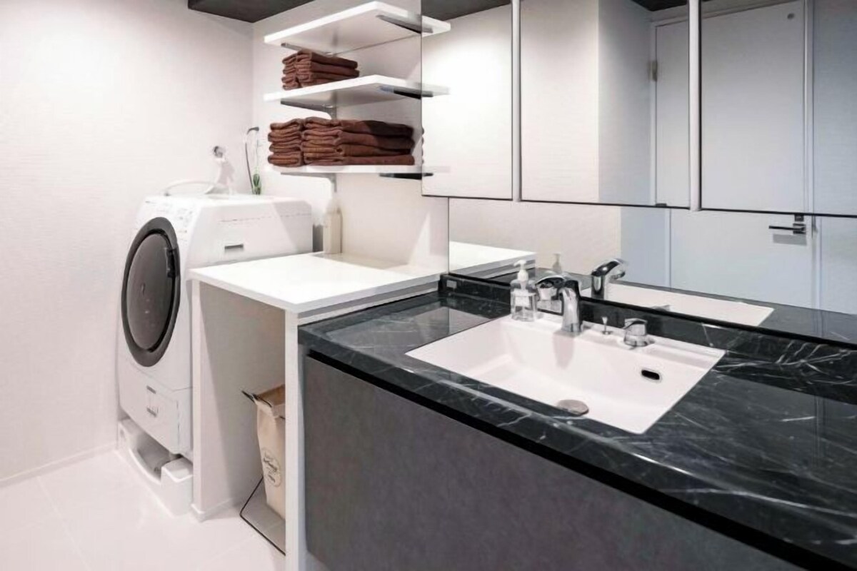 A modern bathroom with a built-in washing machine, a sink with a marble countertop, and shelves for towels.