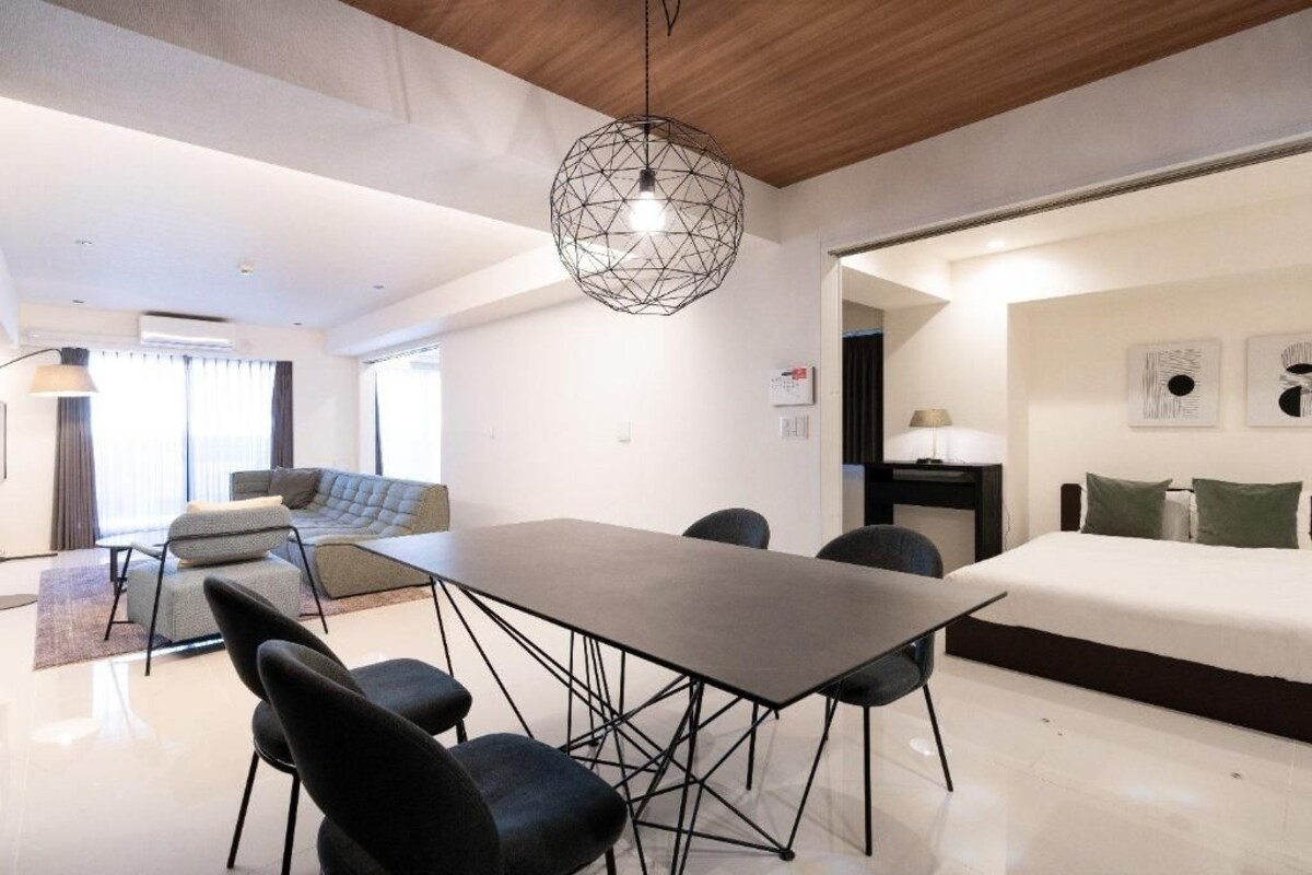 A modern interior with a dining area, a sofa, a bed, and a geometric pendant light.