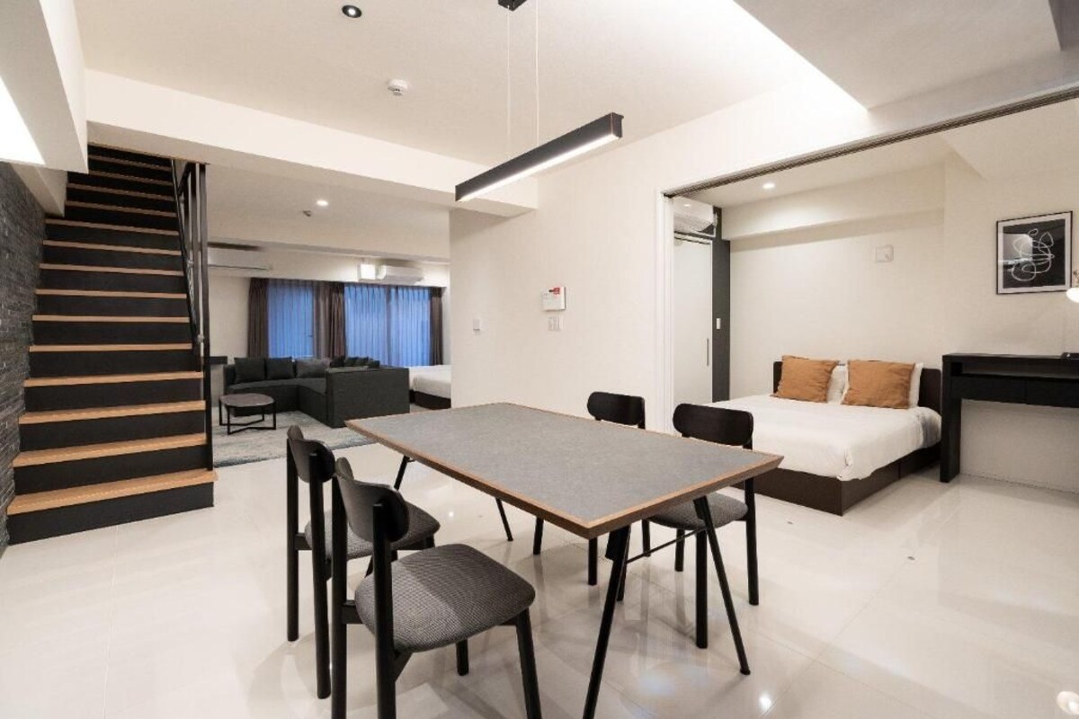 A modern hotel room with a dining area, a bed, and a staircase.