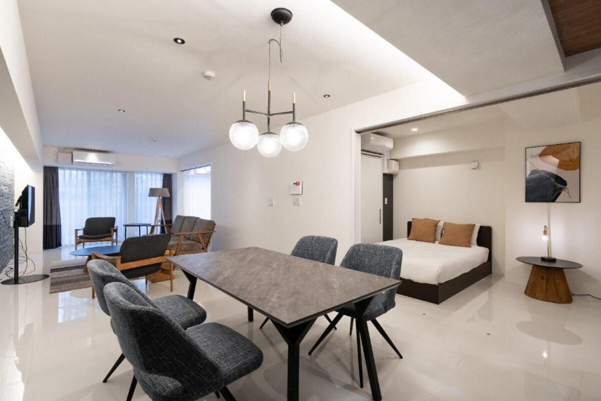 A modern hotel room with a dining area, a bed with two pillows, a round side table, and a large window.