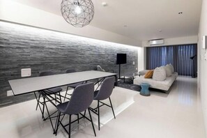 Una sala de estar moderna con una gran mesa de comedor, sillas grises, un sofá blanco con cojines y una lámpara colgante de diseño geométrico.