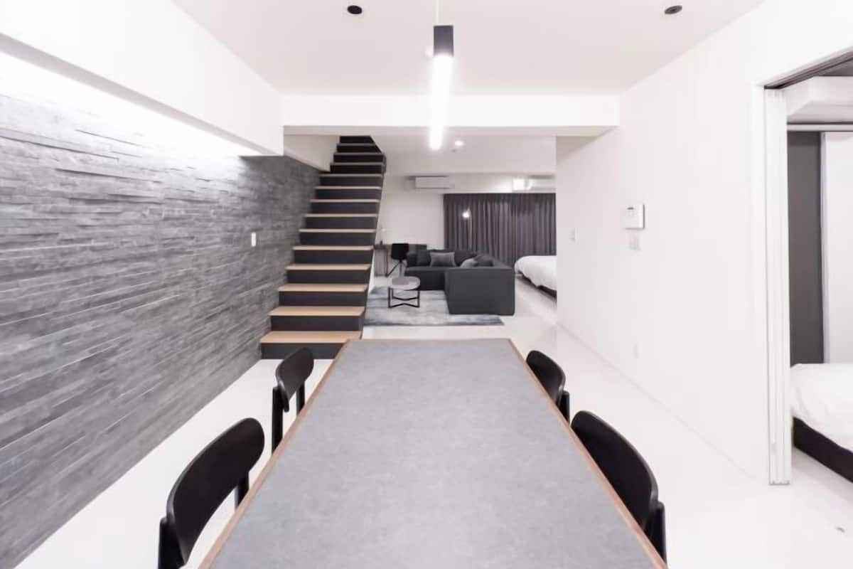 A modern interior with a long table, chairs, a staircase, and a living area with a sofa and curtains.