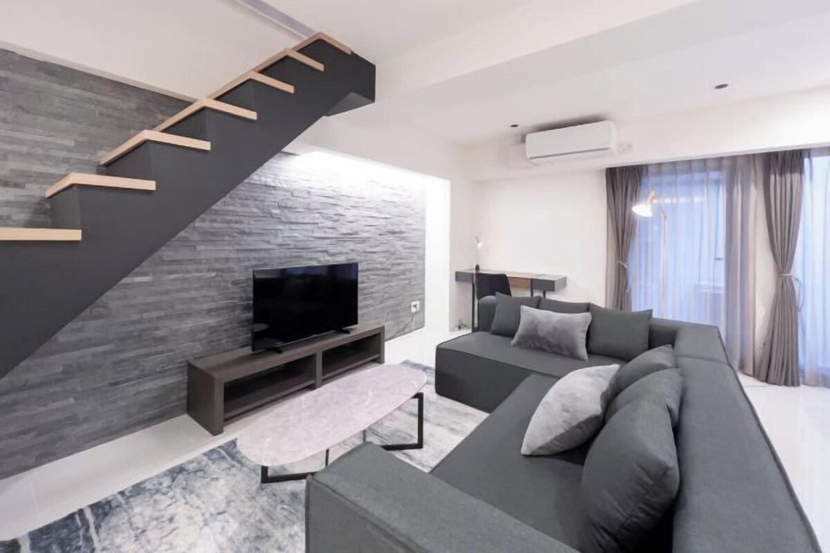 A modern living room with a staircase, a flat-screen TV, a sofa, and a coffee table.
