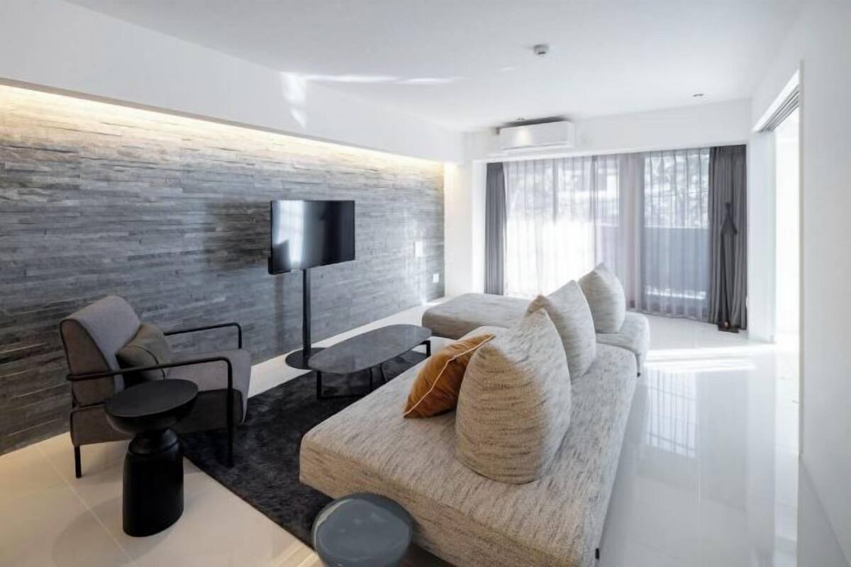 A modern living room with a sofa, armchair, and a flat-screen TV mounted on a textured wall.