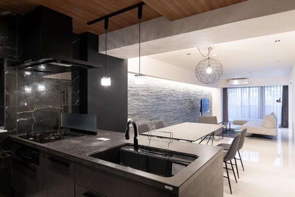 A modern kitchen with a built-in island, a stone backsplash, and a dining area with a table and chairs. - CREAL premier Akasaka (Minato-ku)