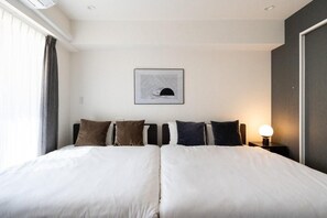 A double bed with white bedding and multiple pillows, a framed artwork above the bed, a bedside lamp, and a window with curtains. - CREAL premier Akasaka (Minato-ku)