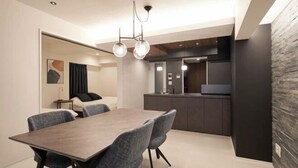 A modern dining area with a wooden table and grey upholstered chairs, a kitchen with dark cabinetry, and a stone accent wall. - CREAL premier Akasaka (Tokyo)