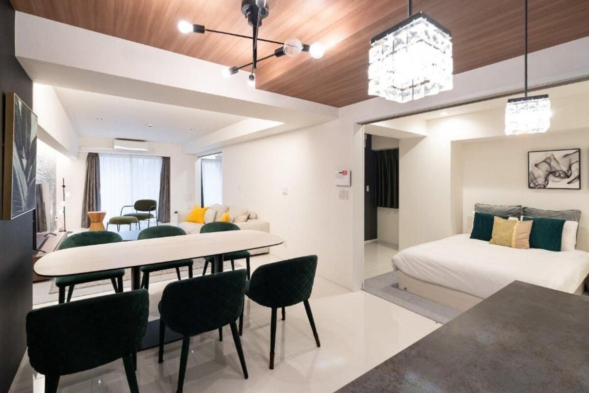 A modern hotel room with a dining area, a bed with a headboard, and a chandelier.