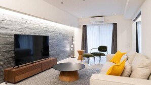 Una sala de estar moderna con un televisor de pantalla plana, una mesa de centro redonda y un sofá con cojines amarillos.