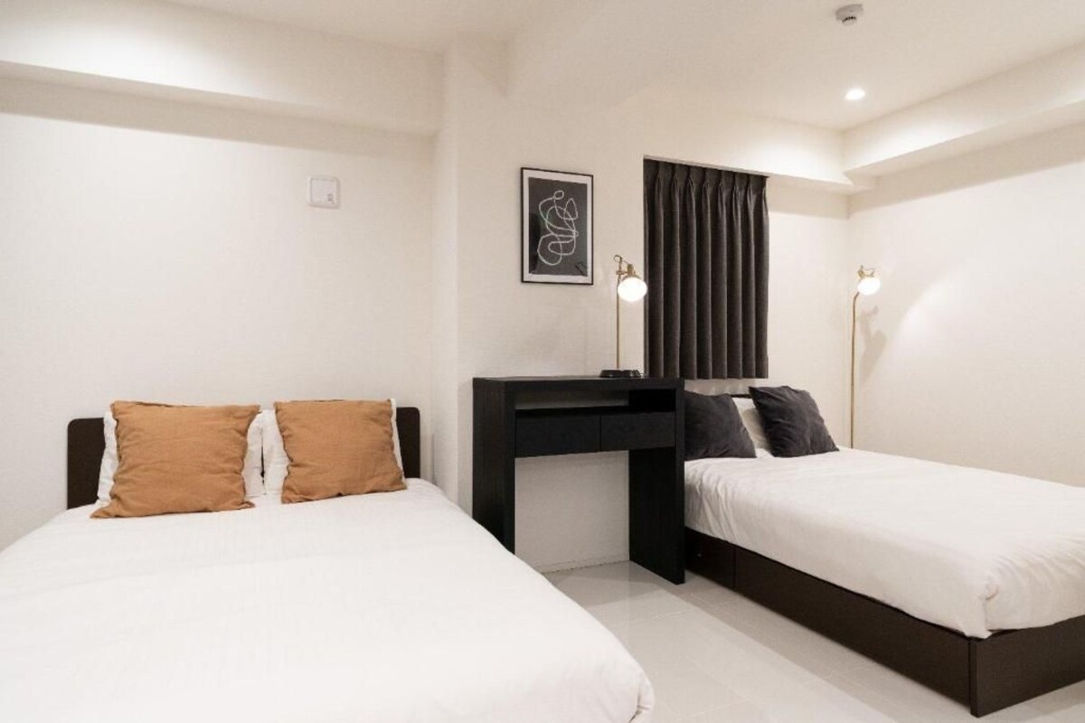 A hotel room with two single beds, a desk, and a chair.