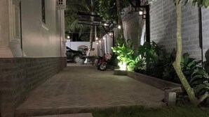 A paved pathway leading to a building with a brick wall and a vehicle parked in the background. - Hotel My Cang (Tra Vinh)